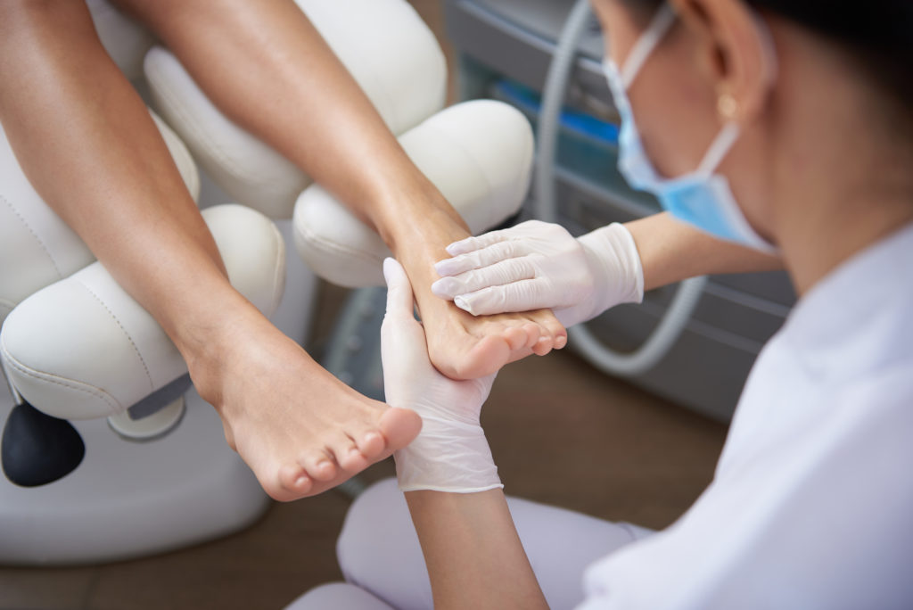 Close up of female hands in white sterile gloves holding lady foot